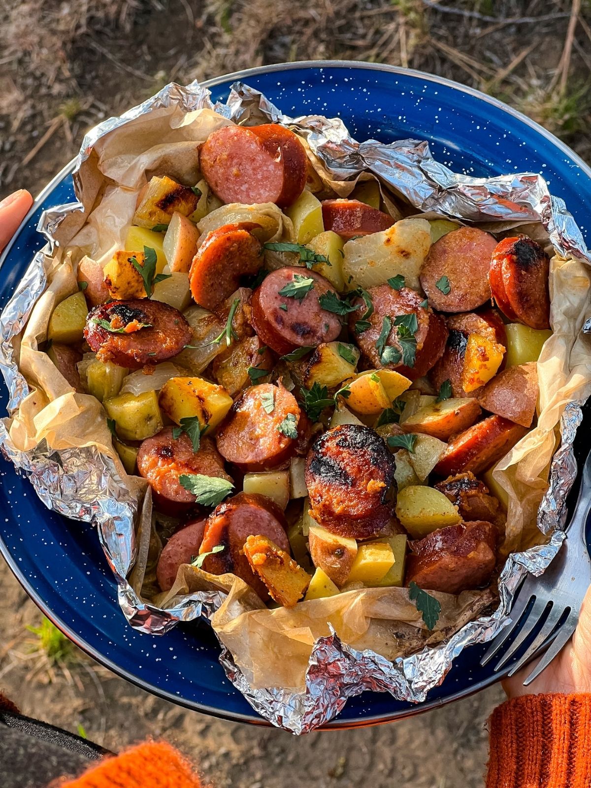 Kielbasa and potato foil packets opened on a plate showing golden sausage slices and tender potatoes with a glossy mustard glaze, garnished with fresh parsley