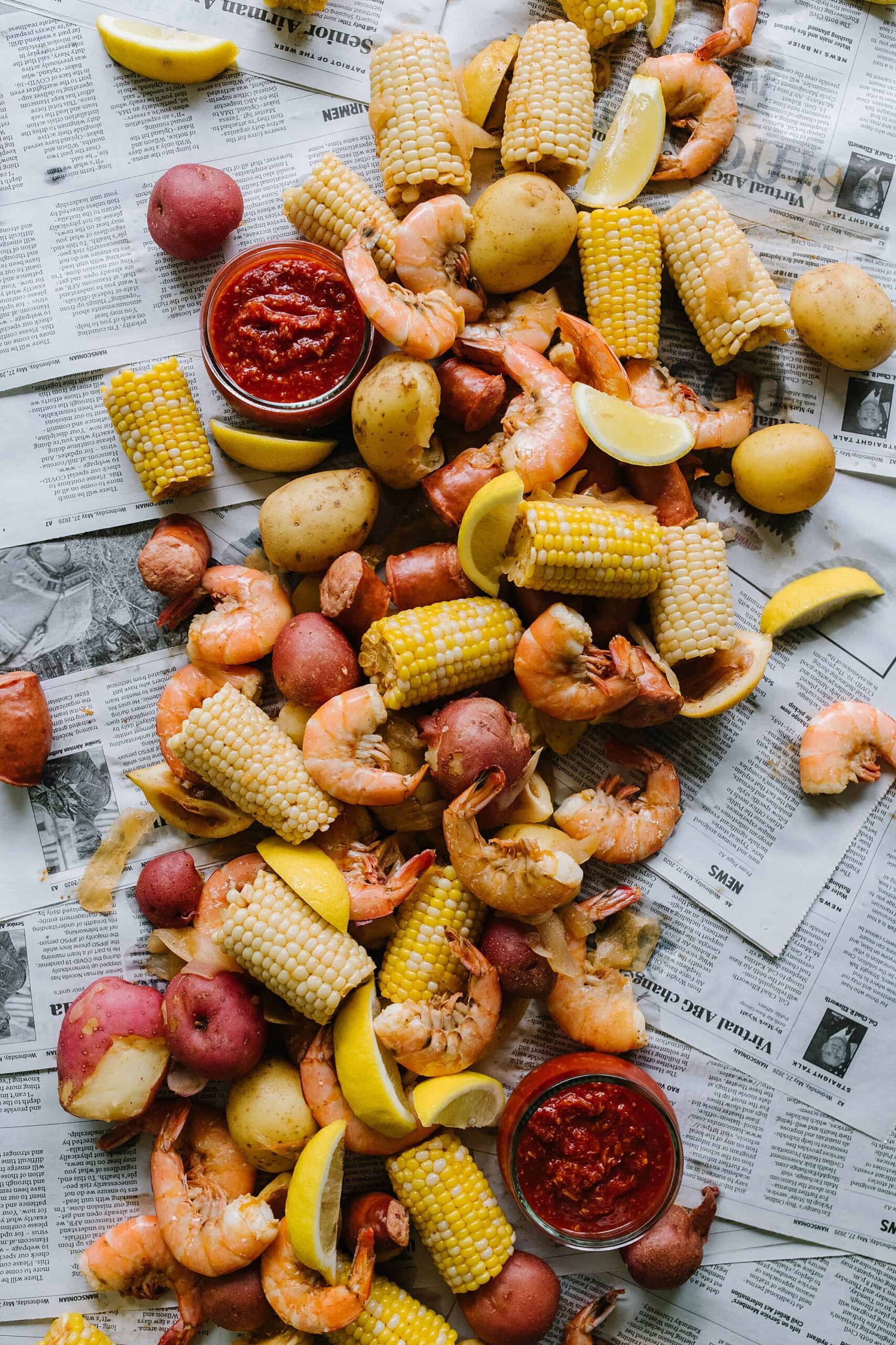 Ingredients for Low Country Shrimp Boil laid out on a wooden surface — raw shrimp, baby red potatoes, corn cobs, andouille sausage, Old Bay seasoning, lemons, and garlic