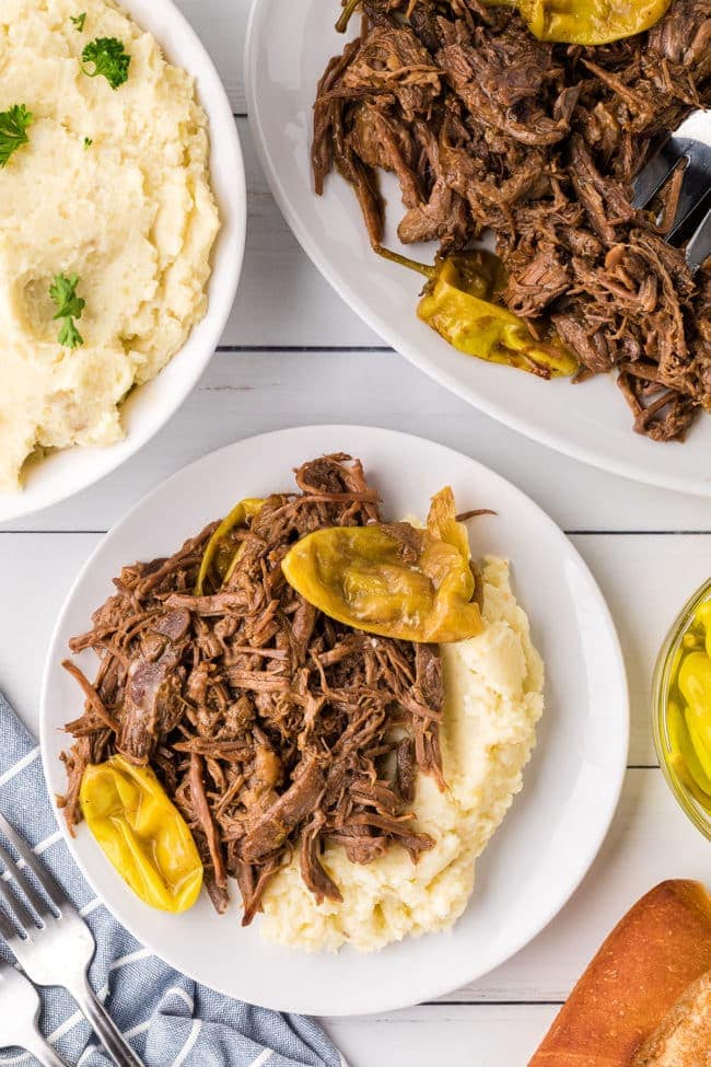 Mississippi Pot Roast served on a white platter with shredded beef, pepperoncini peppers, and rich golden gravy, garnished with fresh parsley