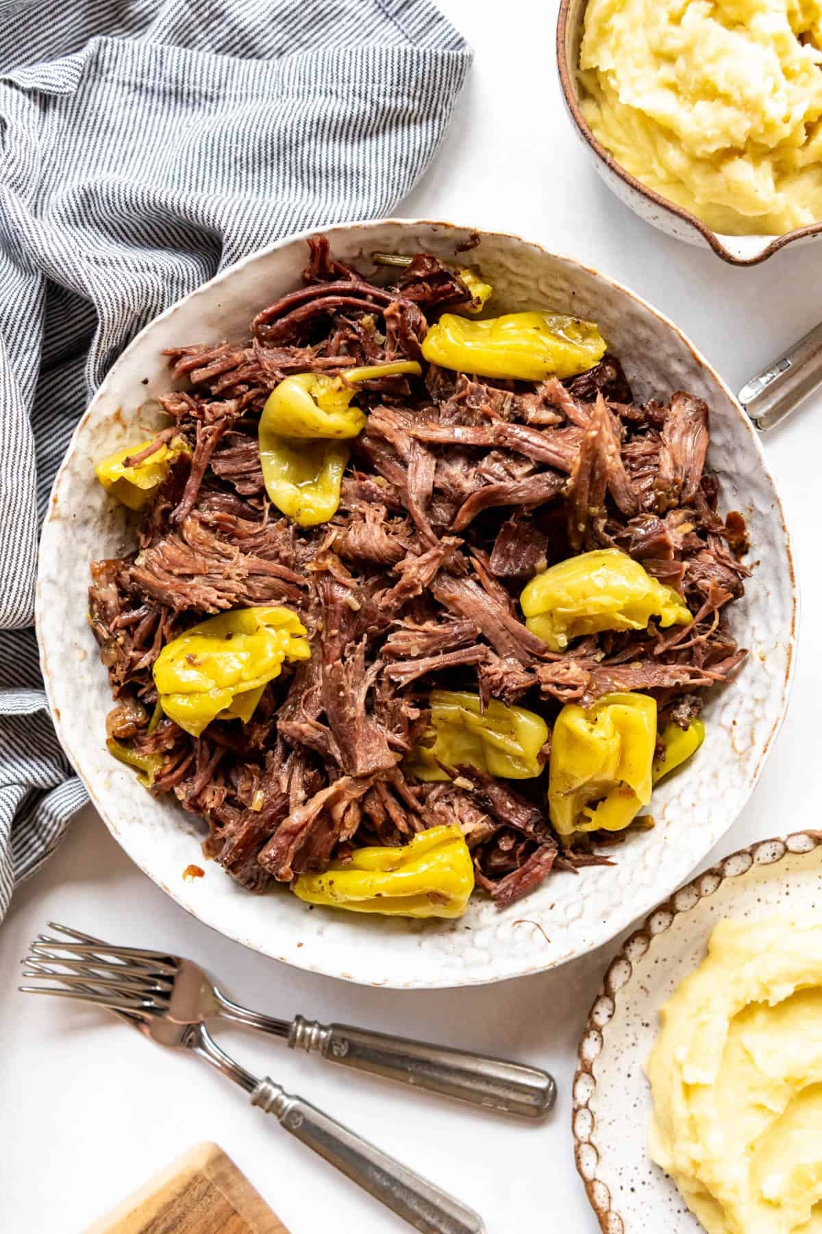 Close-up of shredded Mississippi Pot Roast on creamy mashed potatoes with glossy golden gravy drizzled over the top and a pepperoncini on the side