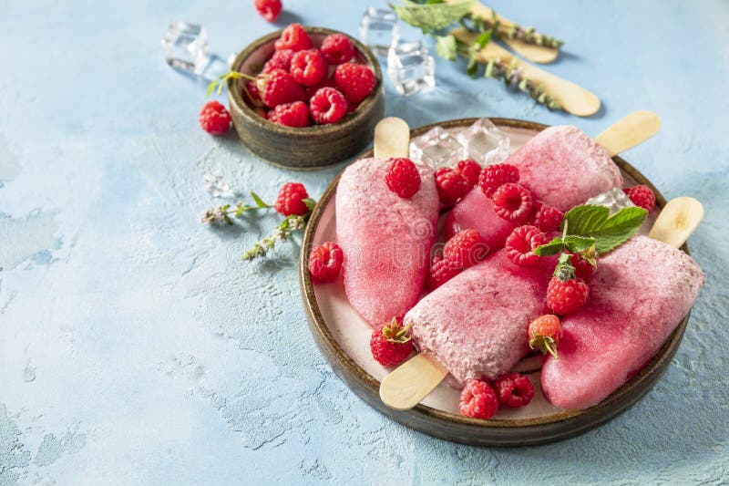 Close-up of a single mixed berry popsicle being held against a bright summer background, showing vivid berry colors and a creamy texture with fruit pieces visible