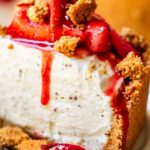 No bake cheesecake on a white cake stand with fresh strawberry topping and golden graham cracker crust, sliced to show creamy filling
