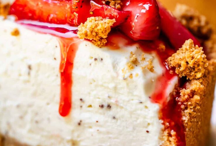 No bake cheesecake on a white cake stand with fresh strawberry topping and golden graham cracker crust, sliced to show creamy filling