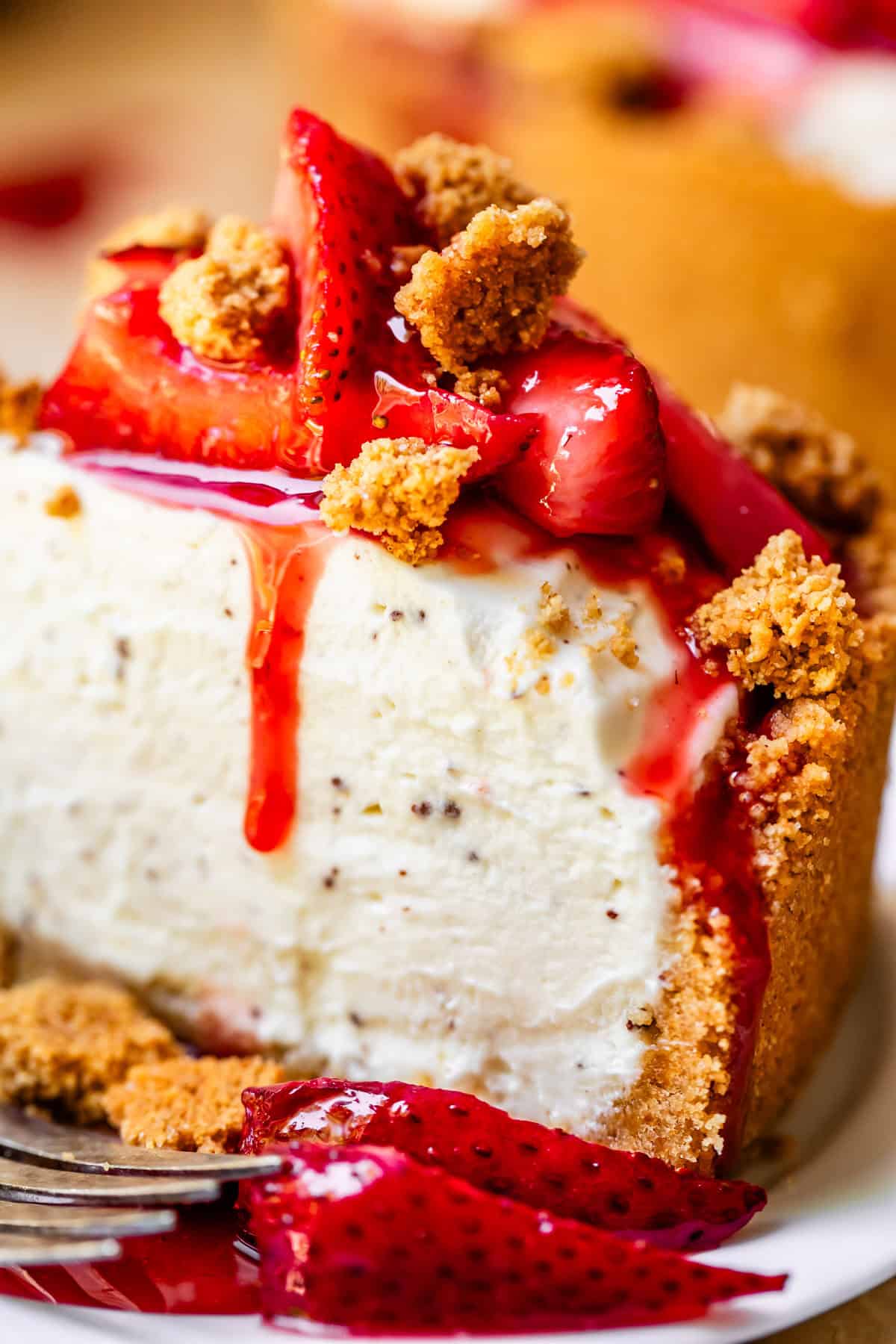 No bake cheesecake on a white cake stand with fresh strawberry topping and golden graham cracker crust, sliced to show creamy filling