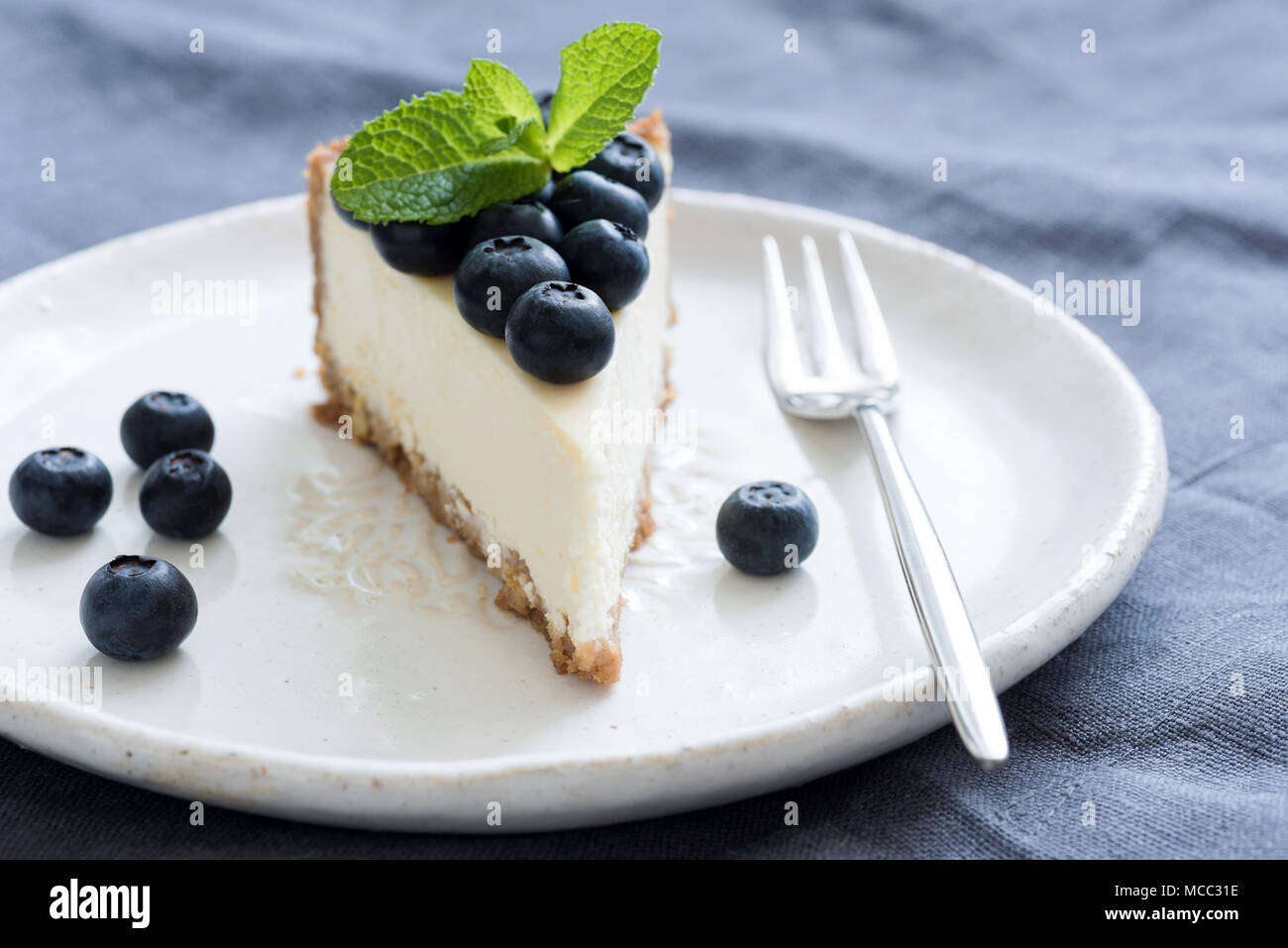 Close-up slice of no bake cheesecake on a white plate topped with fresh mixed berries and a mint sprig, fork resting beside it