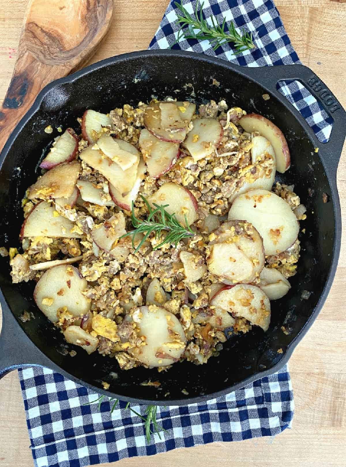 Close-up of a serving of camping breakfast skillet in a rustic enamel camp plate, egg yolk broken and running over golden potatoes and colorful peppers, fresh herbs on top, morning campfire glow in background