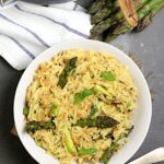 One-pot cheesy orzo with asparagus served in a wide shallow bowl, topped with freshly grated parmesan and cracked black pepper, soft natural light overhead