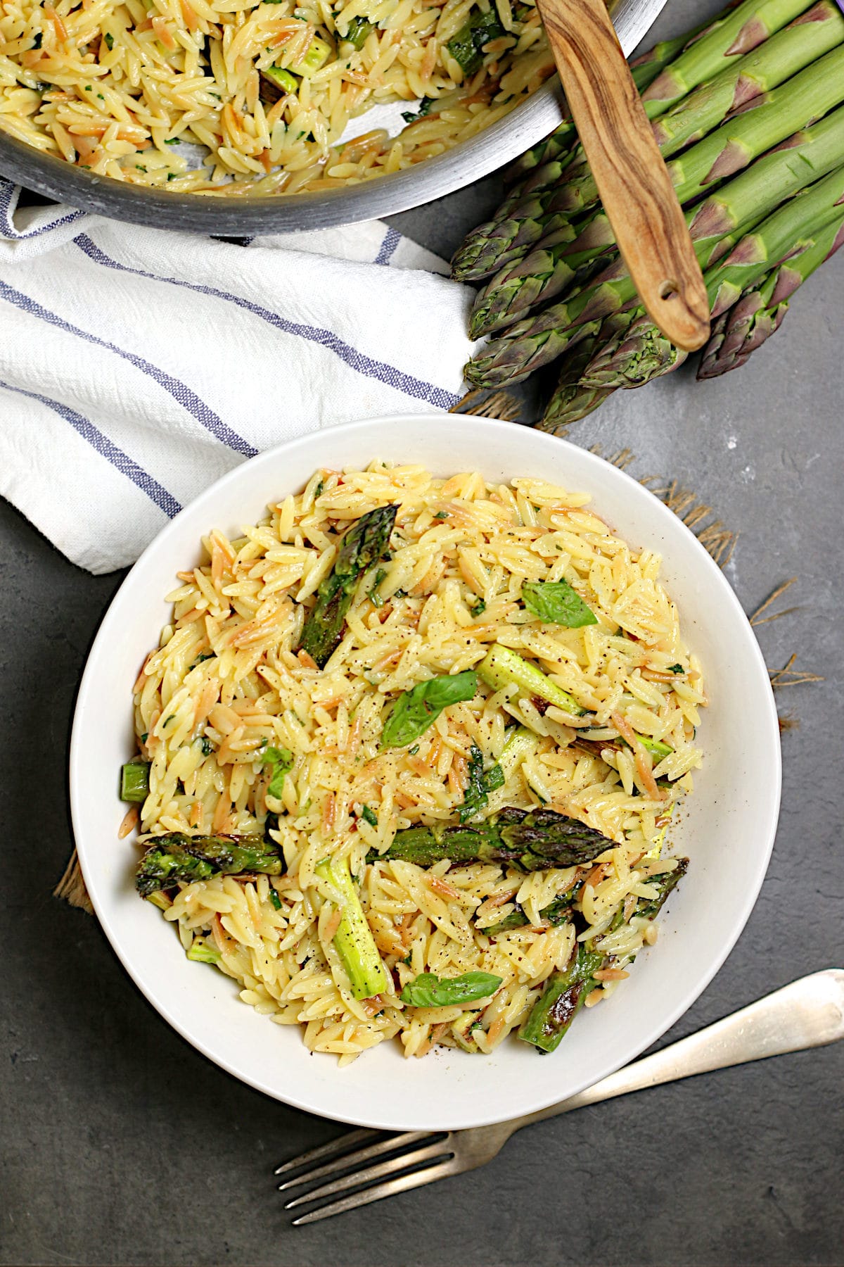 One-pot cheesy orzo with asparagus served in a wide shallow bowl, topped with freshly grated parmesan and cracked black pepper, soft natural light overhead