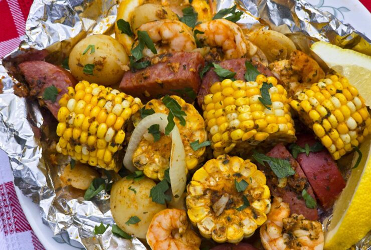 Shrimp boil foil packet opened on a plate showing plump shrimp, smoked sausage slices, golden corn, and baby potatoes garnished with parsley and lemon wedges