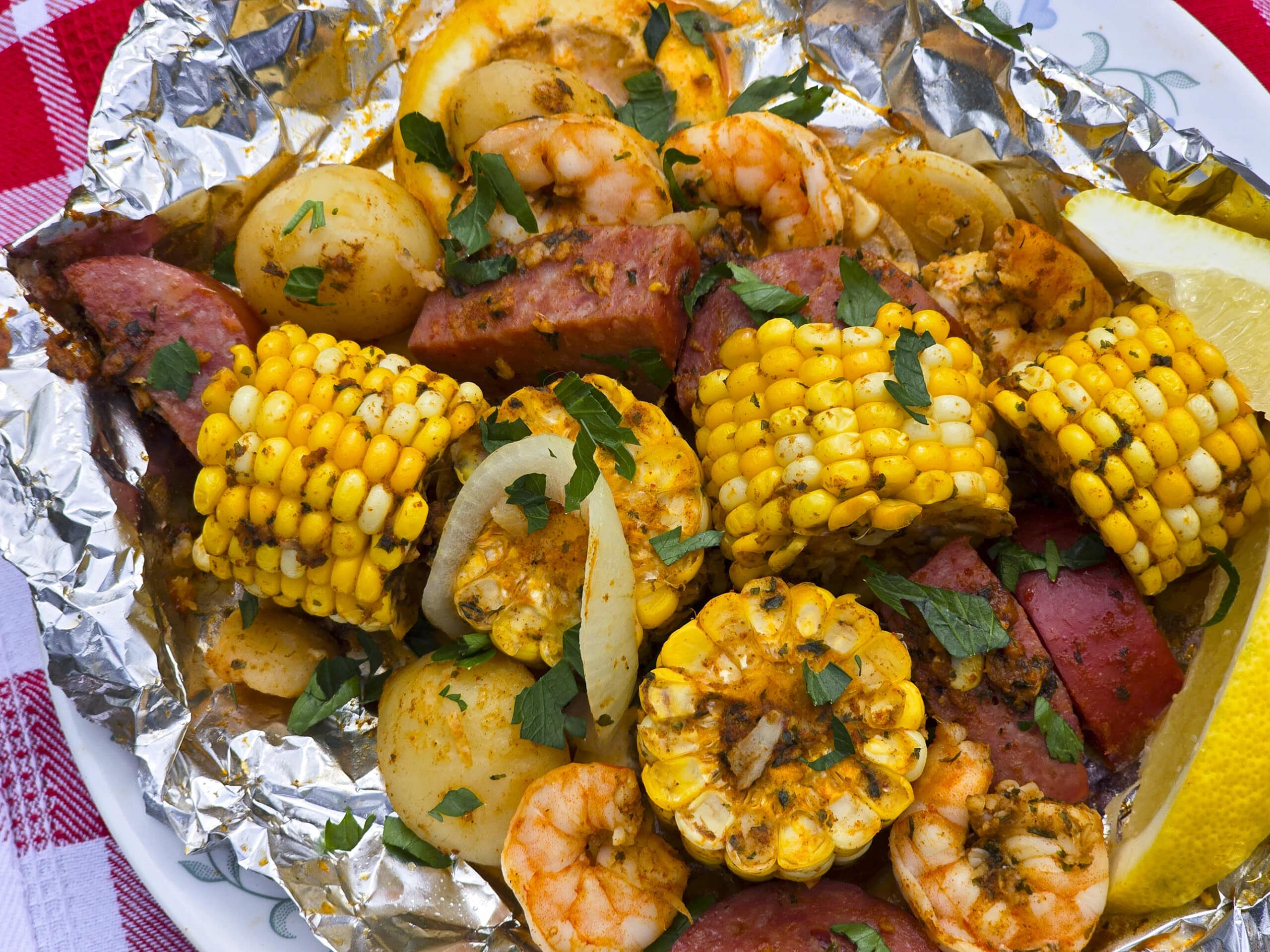 Shrimp boil foil packet opened on a plate showing plump shrimp, smoked sausage slices, golden corn, and baby potatoes garnished with parsley and lemon wedges