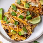 Slow cooker chicken tacos plated beautifully on a wooden board with colorful toppings, lime wedges, and fresh cilantro