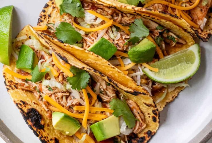 Slow cooker chicken tacos plated beautifully on a wooden board with colorful toppings, lime wedges, and fresh cilantro