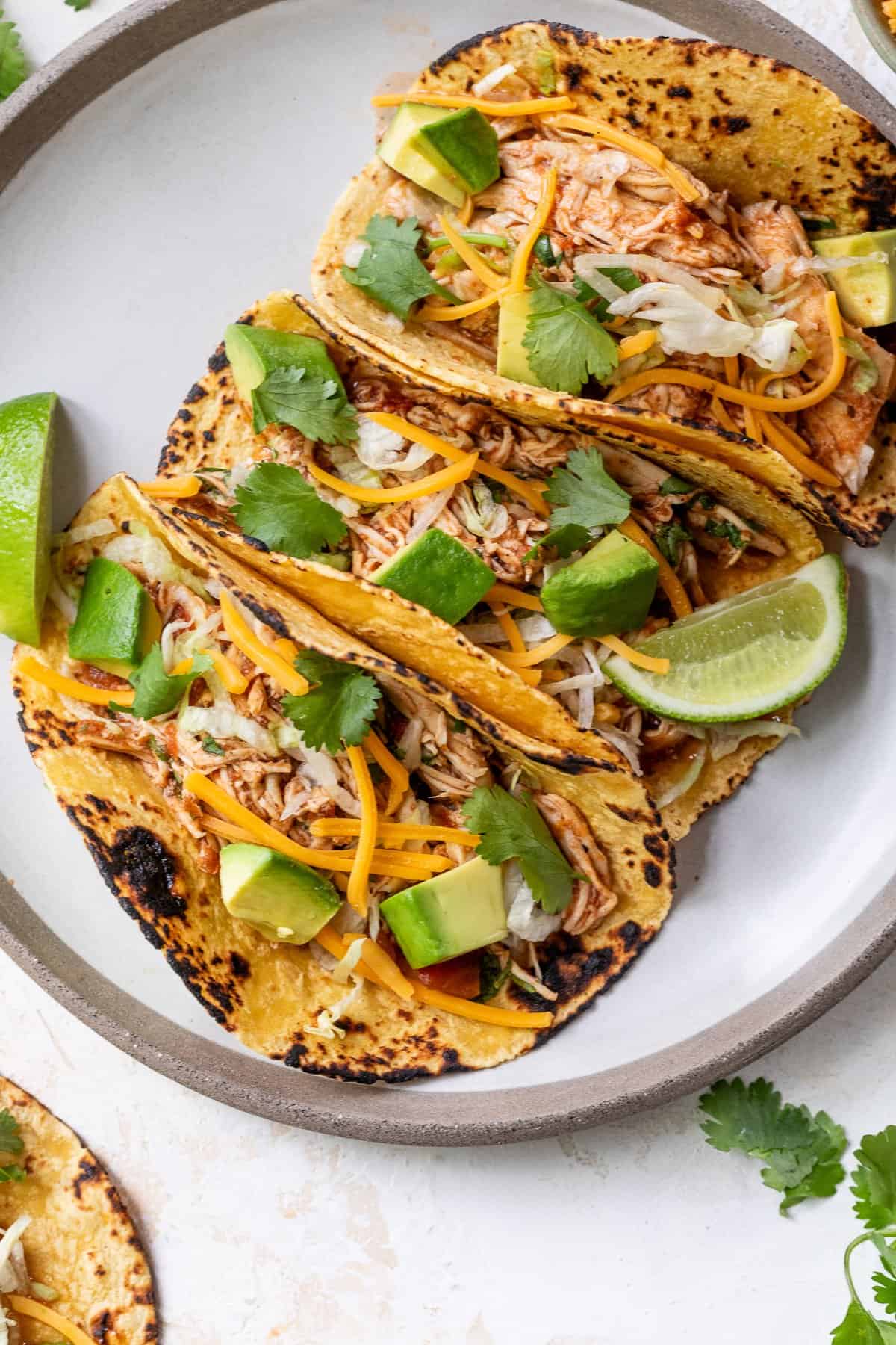 Slow cooker chicken tacos plated beautifully on a wooden board with colorful toppings, lime wedges, and fresh cilantro