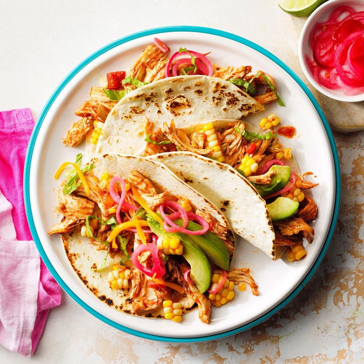Slow cooker chicken tacos ingredients laid out flat on a white surface — raw chicken, spices, canned tomatoes, garlic, onion, lime, and broth
