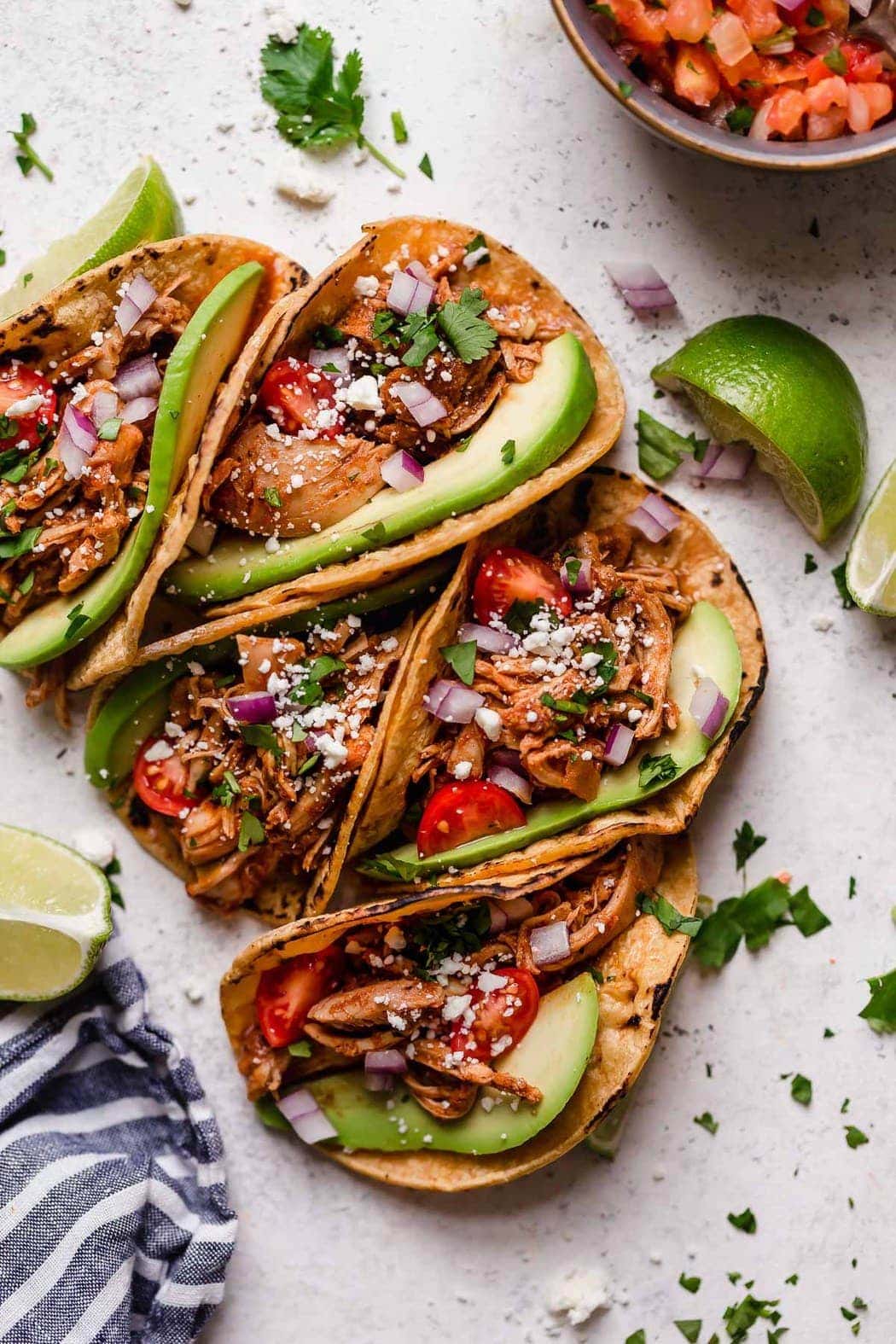 Close-up of a slow cooker chicken taco in a corn tortilla with avocado, pickled red onions, cotija cheese, and fresh cilantro on a rustic wooden surface