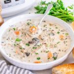 Slow cooker chicken wild rice soup served in a rustic white ceramic bowl, garnished with fresh thyme and cracked black pepper, steam rising, set on a warm wooden table with a linen napkin