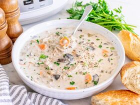 Slow cooker chicken wild rice soup served in a rustic white ceramic bowl, garnished with fresh thyme and cracked black pepper, steam rising, set on a warm wooden table with a linen napkin