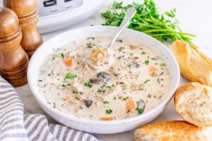 Slow cooker chicken wild rice soup served in a rustic white ceramic bowl, garnished with fresh thyme and cracked black pepper, steam rising, set on a warm wooden table with a linen napkin