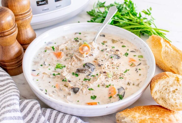 Slow cooker chicken wild rice soup served in a rustic white ceramic bowl, garnished with fresh thyme and cracked black pepper, steam rising, set on a warm wooden table with a linen napkin