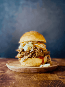 Slow cooker pulled pork served on a toasted bun with coleslaw and pickles, beautifully plated on a rustic wooden board