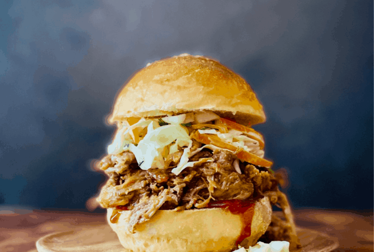 Slow cooker pulled pork served on a toasted bun with coleslaw and pickles, beautifully plated on a rustic wooden board