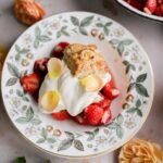Classic strawberry shortcake stacked high with fresh sliced strawberries, fluffy whipped cream, and golden biscuits on a white ceramic plate, photographed in natural light