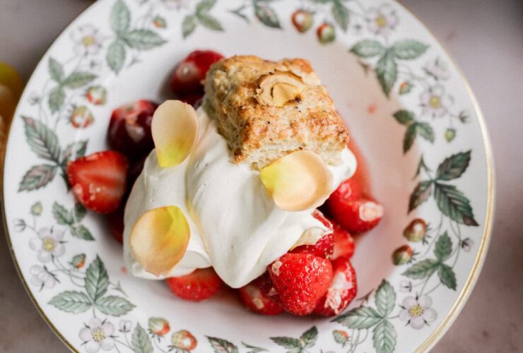 Classic strawberry shortcake stacked high with fresh sliced strawberries, fluffy whipped cream, and golden biscuits on a white ceramic plate, photographed in natural light