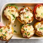 Stuffed bell peppers filled with seasoned ground beef, rice, and melted cheese, beautifully plated on a white dish with fresh herbs garnish