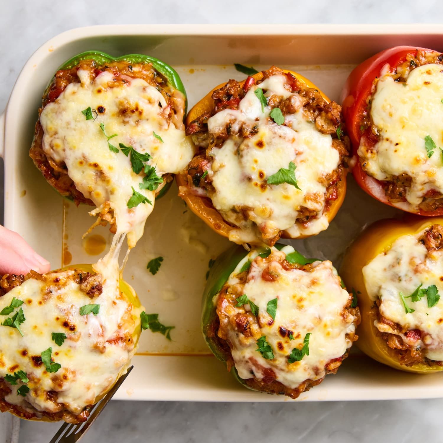Stuffed bell peppers filled with seasoned ground beef, rice, and melted cheese, beautifully plated on a white dish with fresh herbs garnish