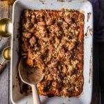 A beautifully plated sweet potato casserole in a white baking dish with a golden pecan brown sugar crust, fresh out of the oven on a rustic wooden table