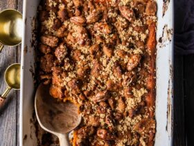 A beautifully plated sweet potato casserole in a white baking dish with a golden pecan brown sugar crust, fresh out of the oven on a rustic wooden table