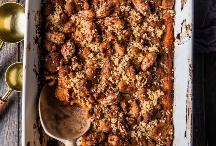 A beautifully plated sweet potato casserole in a white baking dish with a golden pecan brown sugar crust, fresh out of the oven on a rustic wooden table
