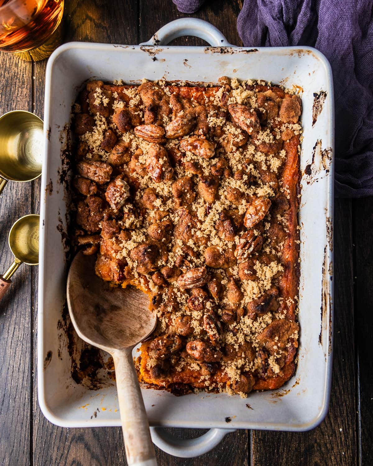A beautifully plated sweet potato casserole in a white baking dish with a golden pecan brown sugar crust, fresh out of the oven on a rustic wooden table