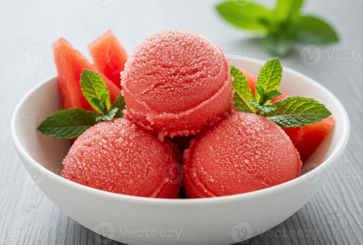 Watermelon sorbet scooped into a white ceramic bowl garnished with fresh mint and a thin watermelon slice, shot overhead on a bright white marble surface with a linen napkin and silver spoon