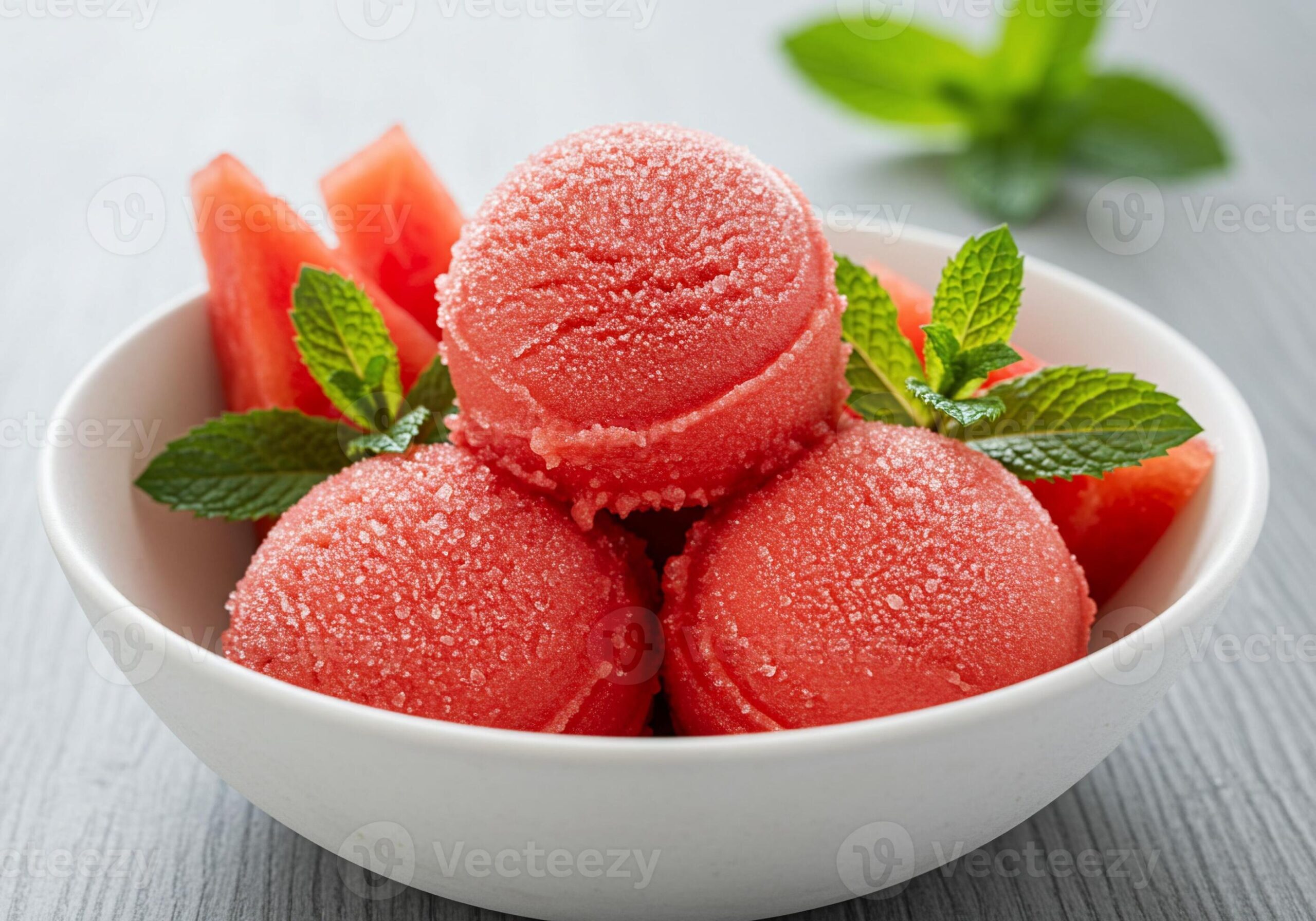 Watermelon sorbet scooped into a white ceramic bowl garnished with fresh mint and a thin watermelon slice, shot overhead on a bright white marble surface with a linen napkin and silver spoon