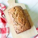 Sliced zucchini bread loaf on a wooden cutting board with a pat of butter melting on the top slice, warm natural light, fresh zucchini in the background