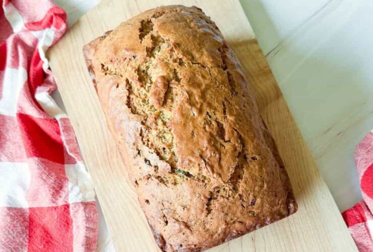 Sliced zucchini bread loaf on a wooden cutting board with a pat of butter melting on the top slice, warm natural light, fresh zucchini in the background