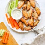 Plate of golden crispy air fryer chicken wings tossed in sauce, garnished with fresh herbs and celery sticks on a rustic wooden board