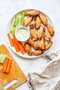 Air Fryer Chicken Wings — Crispy, Juicy, and Healthier Than You Think 13 Plate of golden crispy air fryer chicken wings tossed in sauce, garnished with fresh herbs and celery sticks on a rustic wooden board