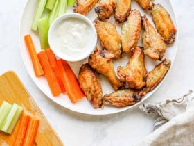 Plate of golden crispy air fryer chicken wings tossed in sauce, garnished with fresh herbs and celery sticks on a rustic wooden board