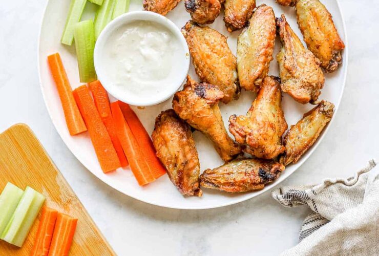 Plate of golden crispy air fryer chicken wings tossed in sauce, garnished with fresh herbs and celery sticks on a rustic wooden board