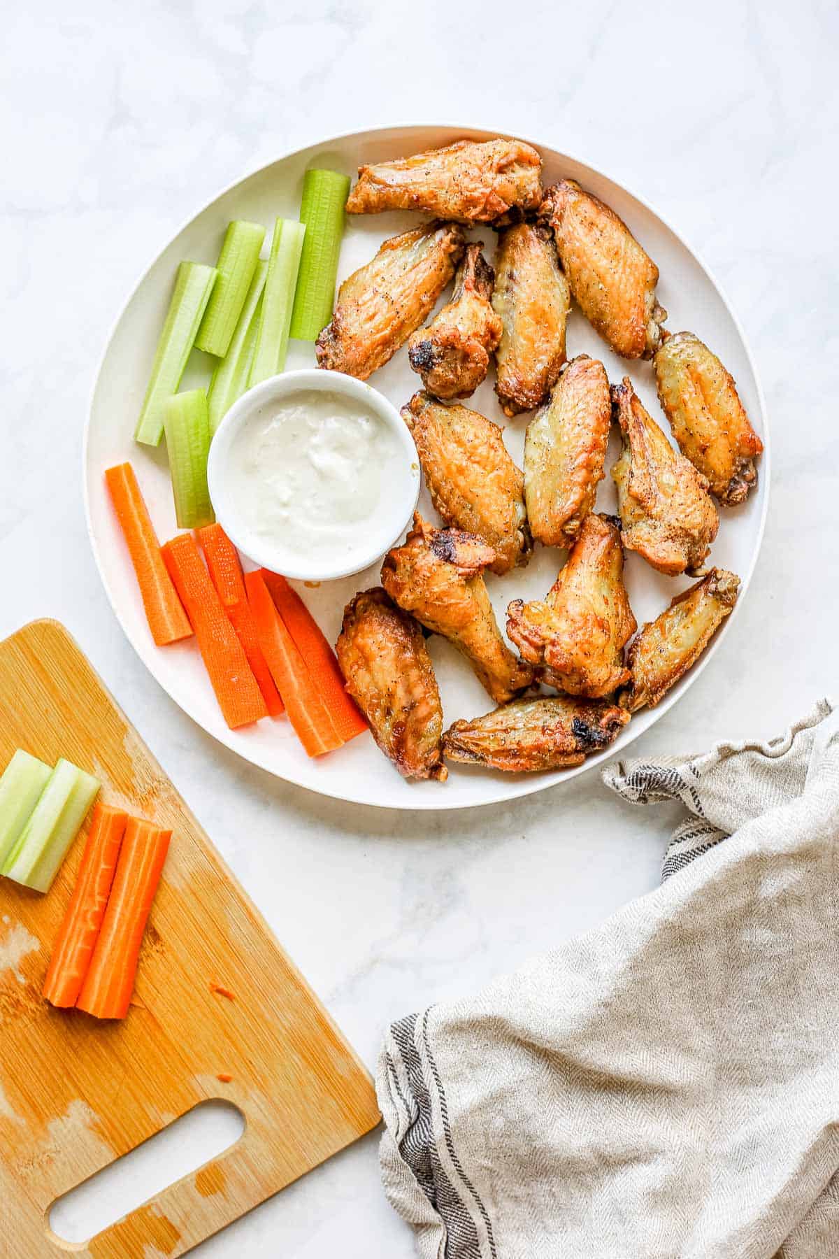 Plate of golden crispy air fryer chicken wings tossed in sauce, garnished with fresh herbs and celery sticks on a rustic wooden board
