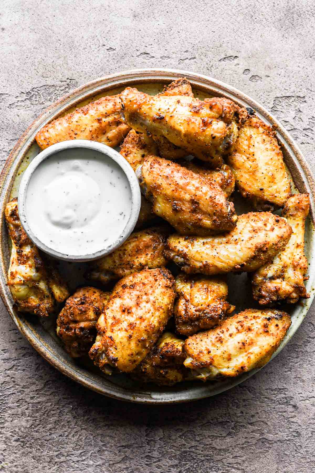 Close-up of chicken wings being pat dried with paper towels next to small bowls of dry rub spices — baking powder, garlic powder, smoked paprika — on a clean marble countertop
