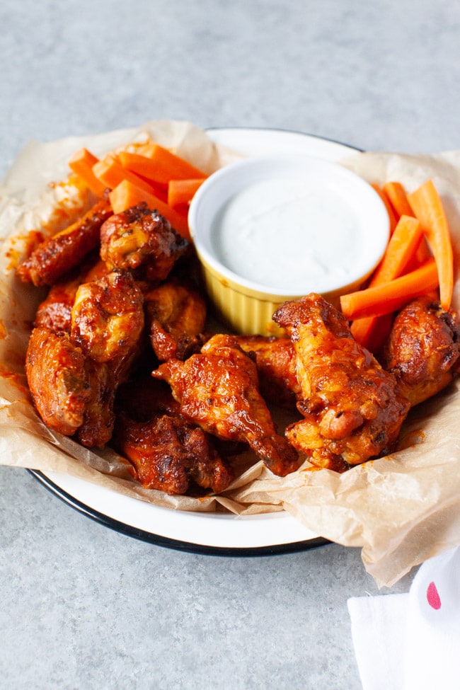 Close-up of a hand holding a crispy golden air fryer chicken wing with sauce glaze, celery and blue cheese dip visible in the background on a wooden board