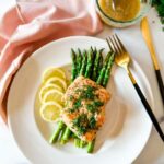 Air fryer salmon fillets plated beautifully on a white dish with lemon slices, fresh dill, and a side of roasted asparagus