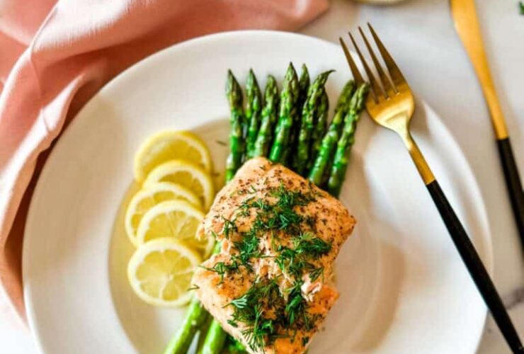 Air fryer salmon fillets plated beautifully on a white dish with lemon slices, fresh dill, and a side of roasted asparagus