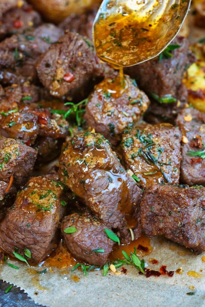 Close-up of air fryer steak bites glistening with garlic butter, garnished with fresh thyme and flaky sea salt, served in a cast iron skillet