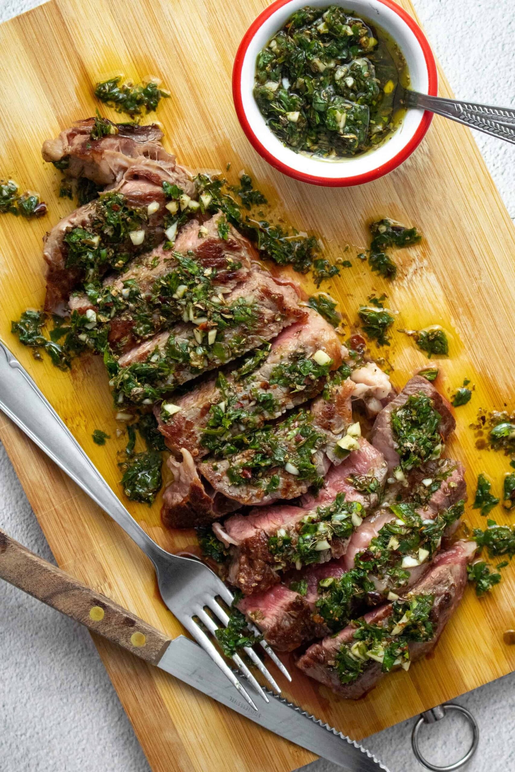 Argentinian chimichurri steak sliced on a wooden board with bright green chimichurri sauce drizzled over the top, fresh parsley garnish, and a rustic linen napkin beside it