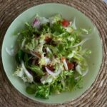 Overhead shot of Asian spiralized cucumber noodle salad in a wide bowl, garnished with sesame seeds, sliced scallions, shredded carrots, and a drizzle of sesame-ginger dressing on a light linen surface