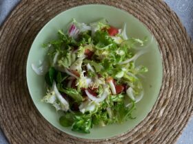 Overhead shot of Asian spiralized cucumber noodle salad in a wide bowl, garnished with sesame seeds, sliced scallions, shredded carrots, and a drizzle of sesame-ginger dressing on a light linen surface
